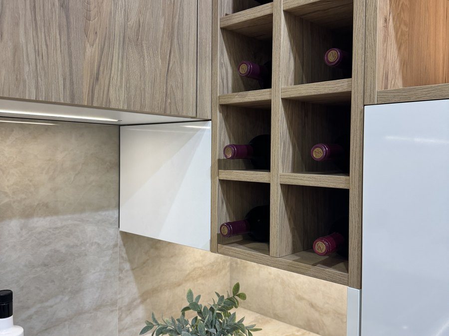 Botellero de madera integrado entre los muebles altos de una cocina con frontal efecto piedra