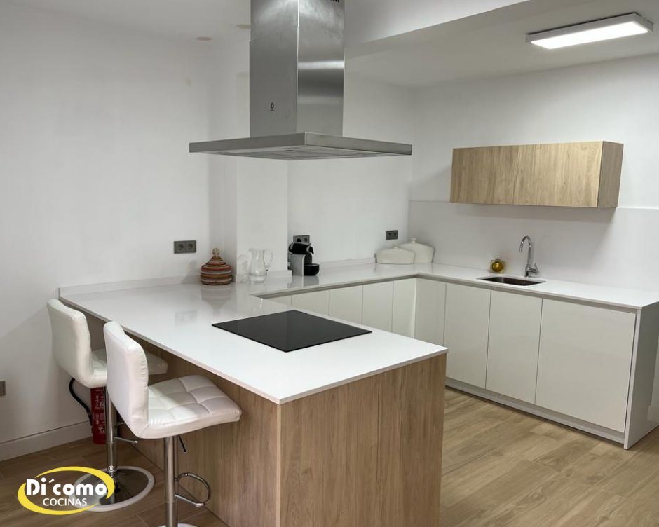 Cocina blanca con península de encimera blanca sobre base de madera y taburetes blancos