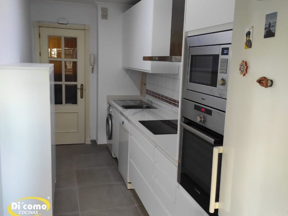 Cocina lineal blanca con microondas y horno integrados en columna junto a la puerta