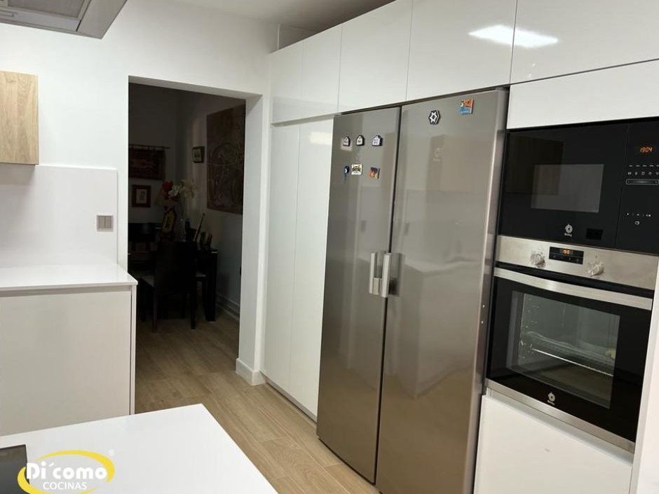 Mueble para microondas en columna blanca, con el microondas encima del horno junto a un frigorífico americano