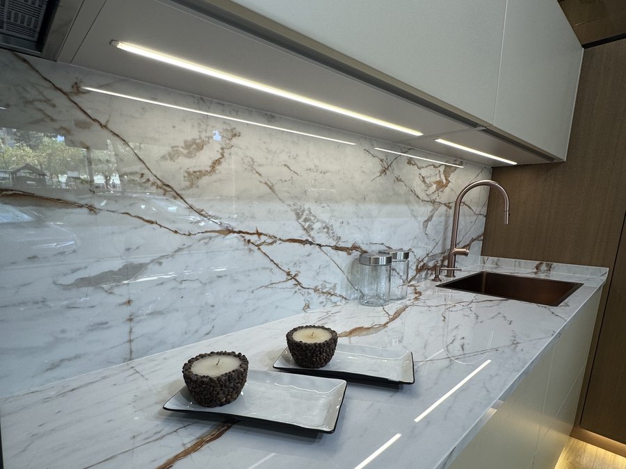 Iluminación LED bajo mueble reflejada en la encimera de mármol, junto a grifo en acabado cobre